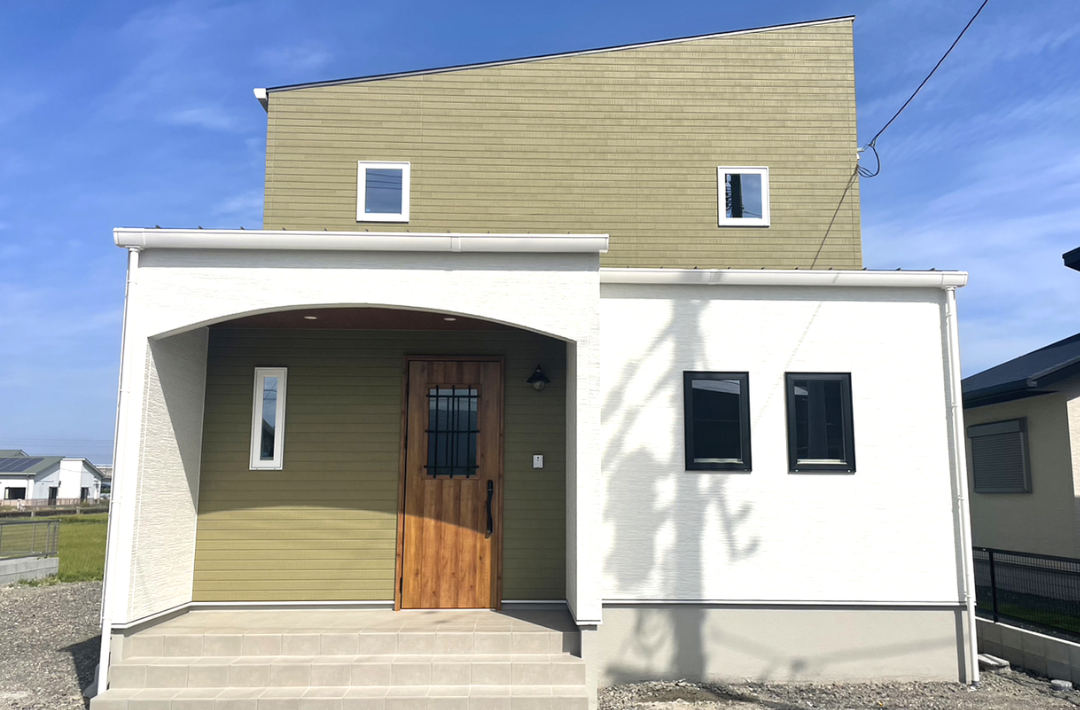 木目とグリーンの外壁に白い立体的な造形が映える片流れ屋根の2階建て